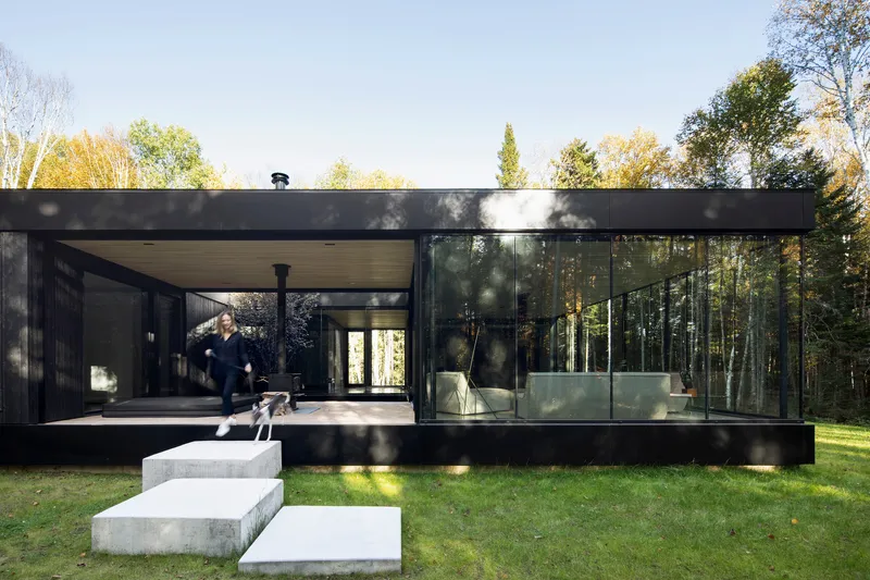 Glass facade with concrete terrace steps and a figure walking under dappled sunlight