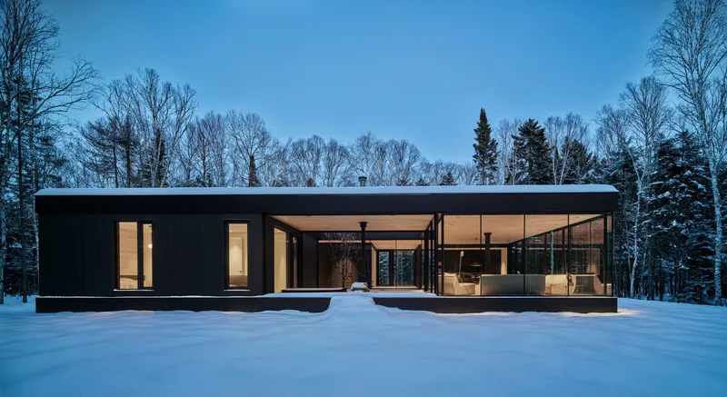 Flat roofed pavilion in deep snow with interior lights glowing under blue twilight