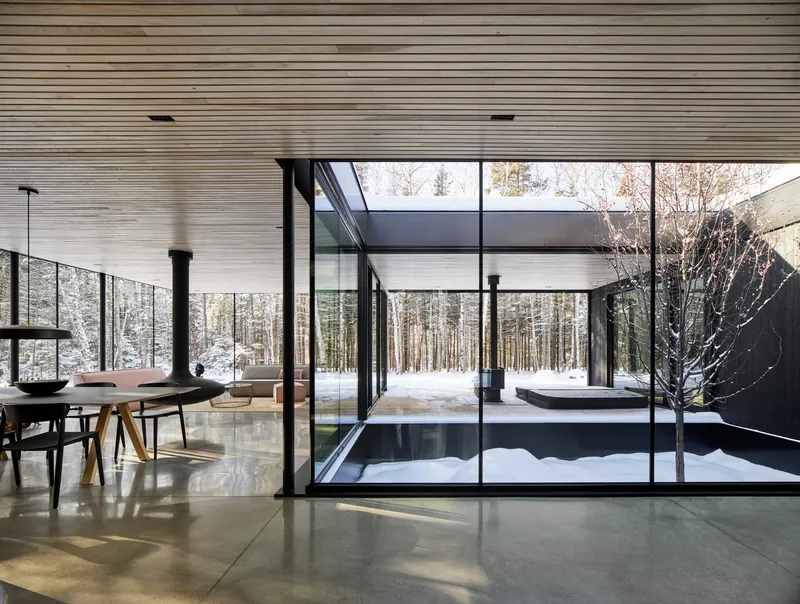 Interior view through black-framed glazing toward central courtyard with tree and snow beyond