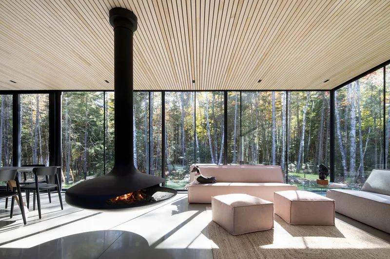 Living space with freestanding fireplace beneath radial slatted ceiling flooded with sunlight from the forest