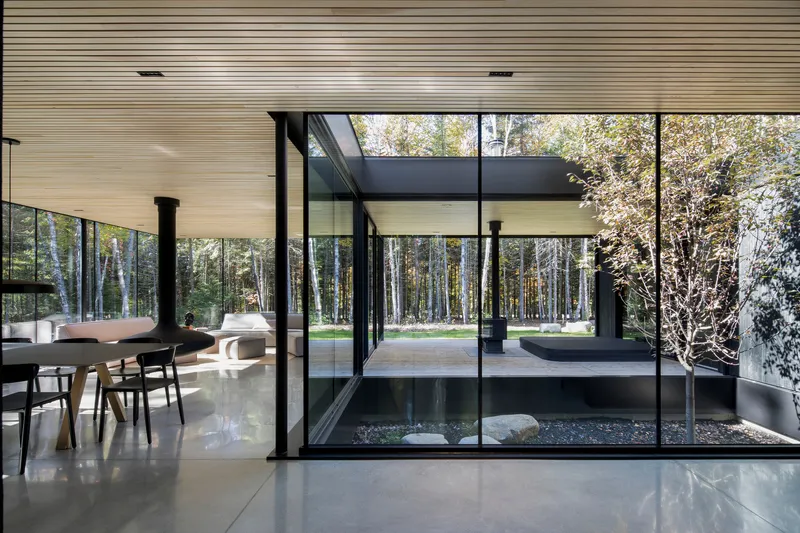 View across polished floor toward glazed courtyard with single tree planted among dark gravel