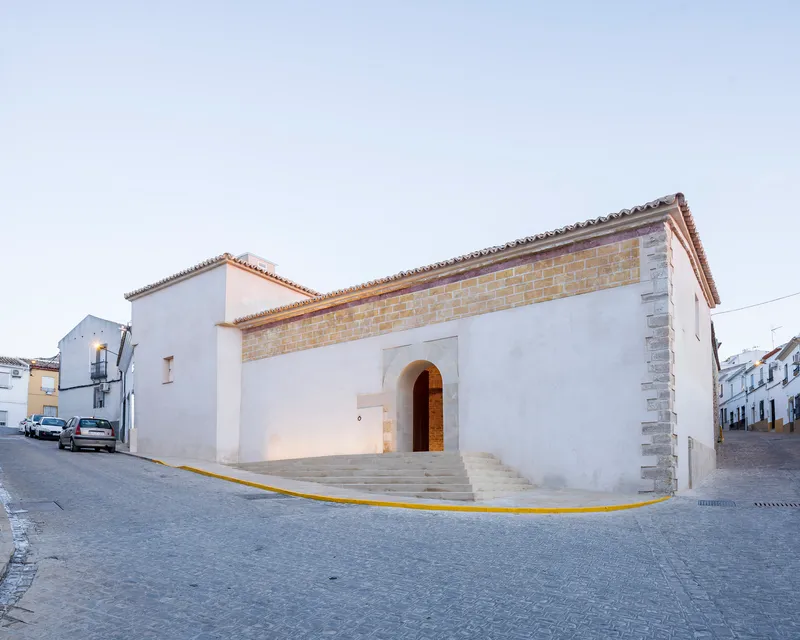 Street corner view of the white stucco facade with arched entry and terra cotta tile roof at dusk