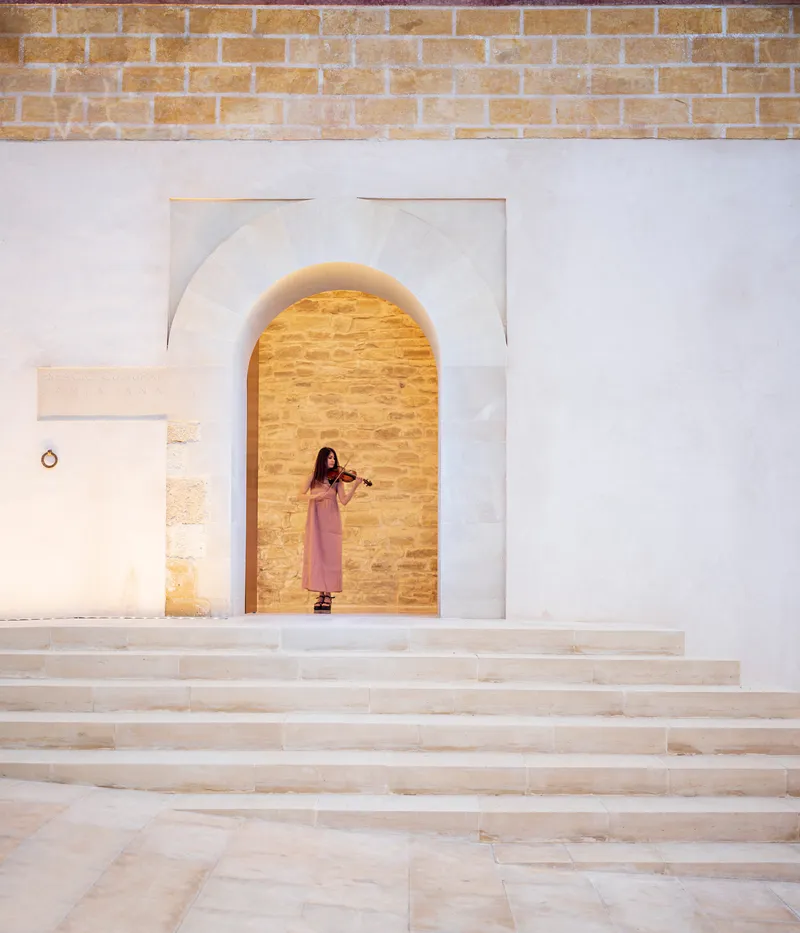 Wide stone steps leading to an arched opening in a white plaster wall with a violinist standing inside