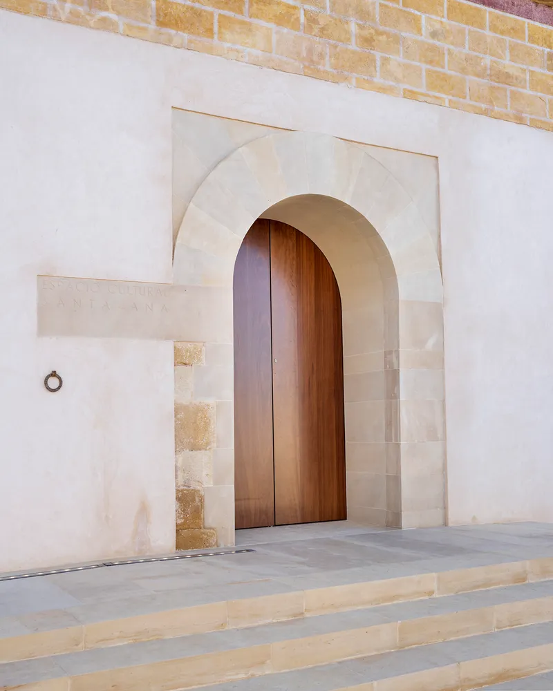Arched timber entry door framed by limestone voussoirs set within a white stucco facade above stone steps