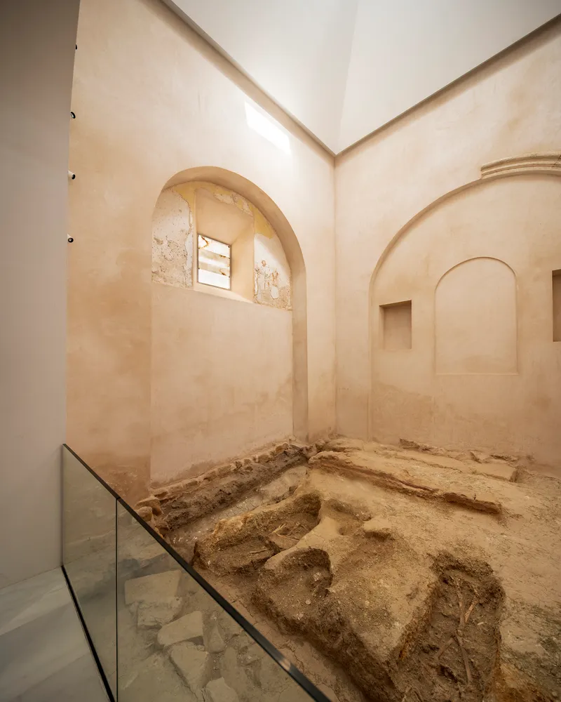 Interior view of restored arched chamber with exposed archaeological remains protected by a glass barrier