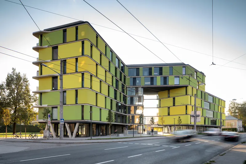 Streetside view of the yellow and green panelized facade on pilotis with overhead tram wires at dusk