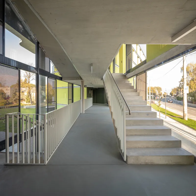 Ground-level circulation corridor with concrete stairs and exposed ceiling slab opening to the yellow facade