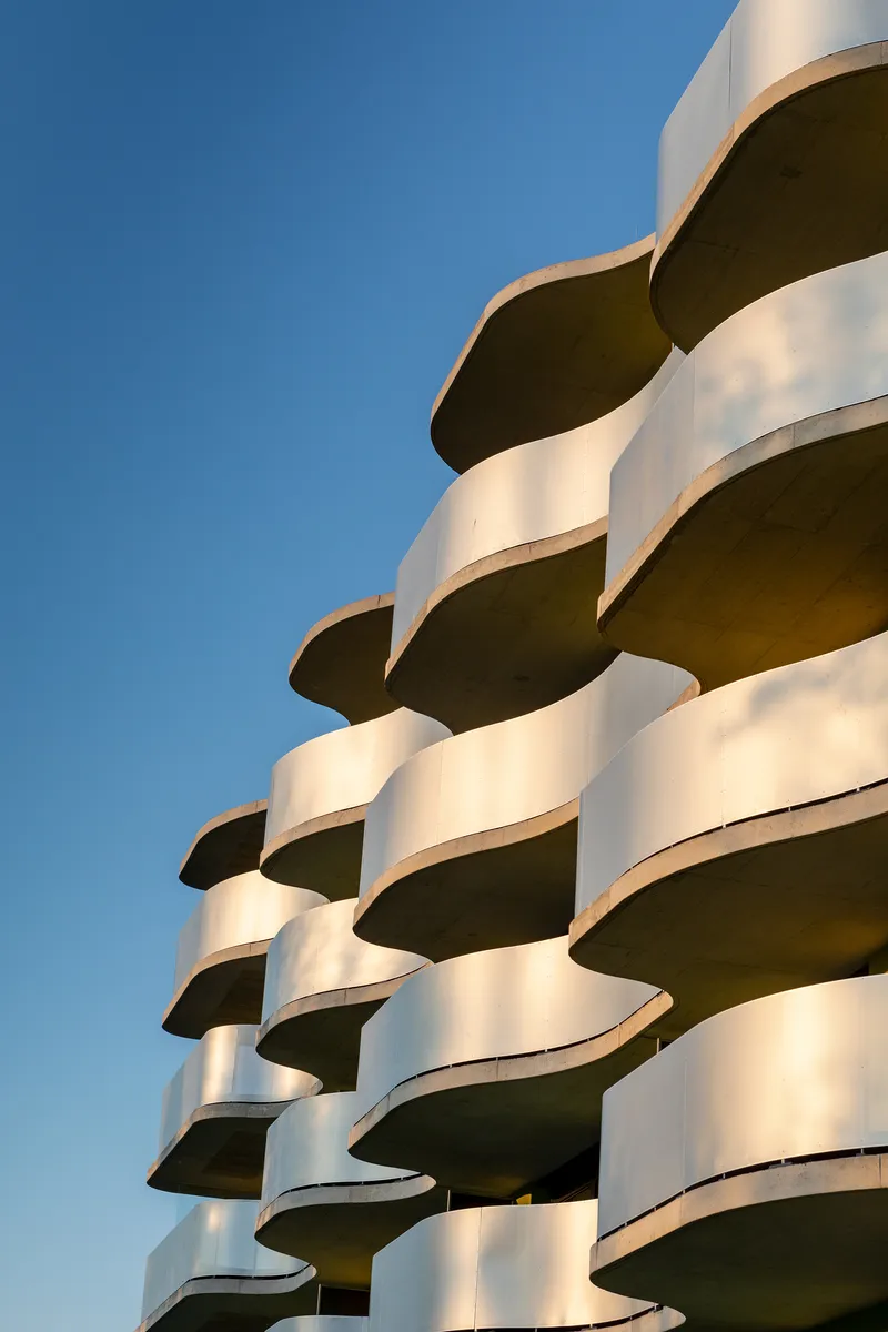 Stacked white concrete balconies with curved edges casting deep shadows under clear blue sky