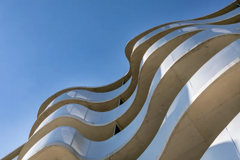 Upward view of layered concrete ribs forming wavelike balcony edges against blue sky
