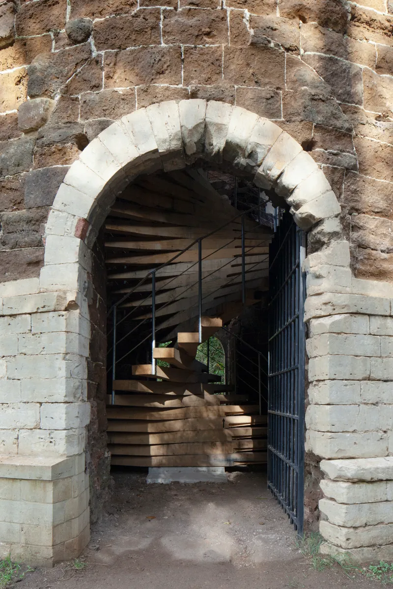 Stone archway with white voussoirs framing a timber staircase and open metal gate beyond