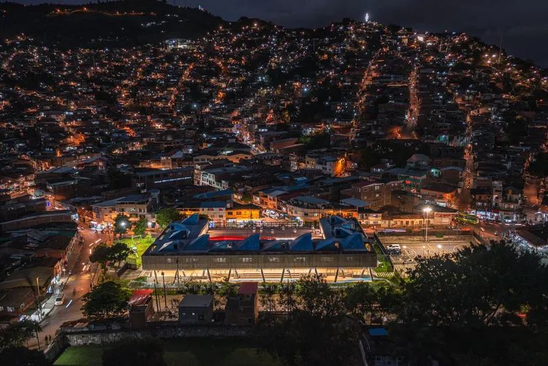 Nighttime aerial view of illuminated compound with blue roof volumes nestled in hillside residential district
