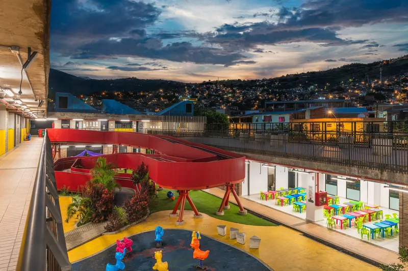 Central courtyard with red curved canopy over playground at dusk with surrounding hillside lights