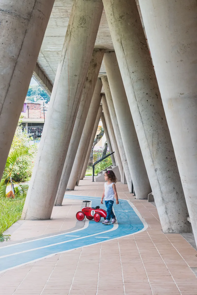 Covered walkway with angled concrete columns and blue painted floor markings where a child plays