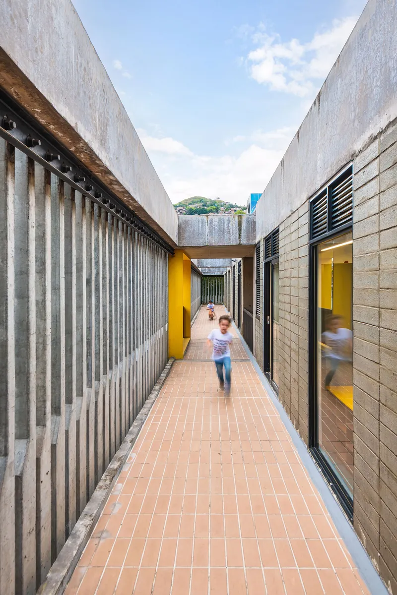 Child running through a narrow corridor with corrugated metal walls and yellow-lit openings
