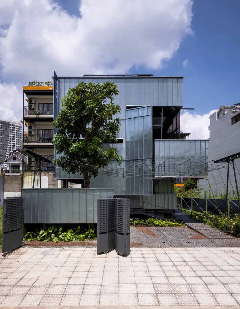 Front elevation showing the stacked metal-clad volumes with a tree emerging through the lower levels