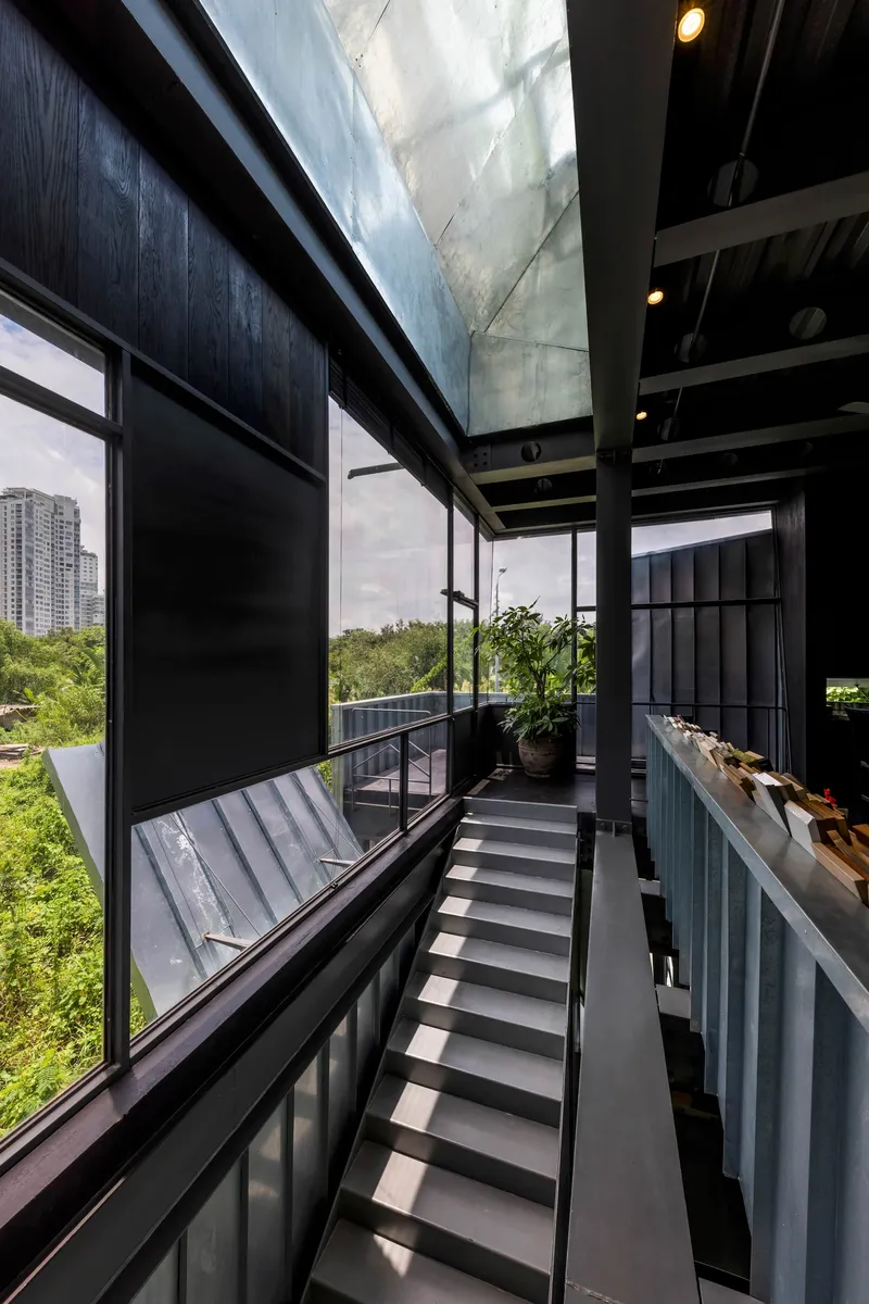 Interior staircase with metal treads and exposed steel beams beneath a concrete skylight shaft