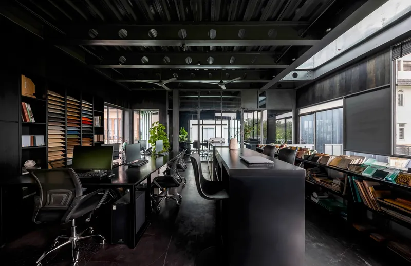 Open-plan office interior with exposed steel trusses, black furnishings and material sample shelving