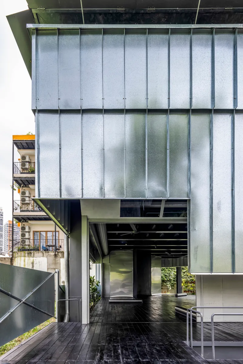Vertical corrugated metal facade with deep overhang sheltering the timber deck entrance