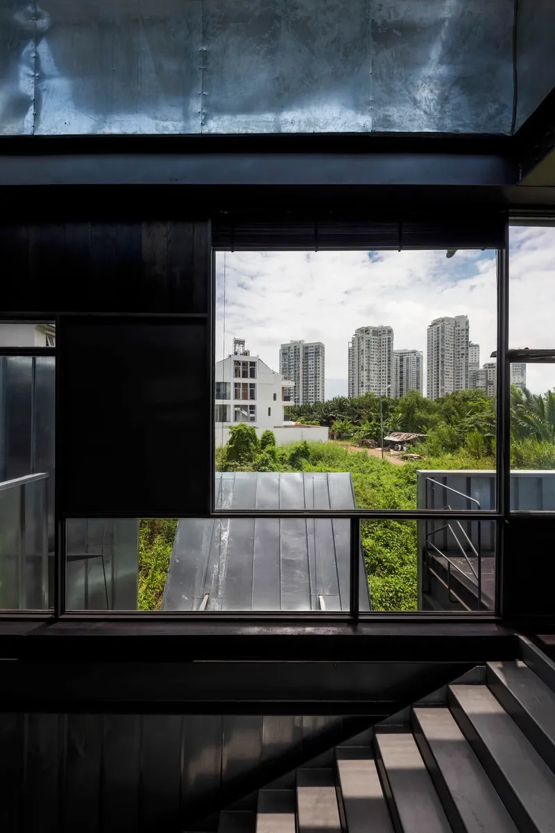 Large window opening framed by blackened steel beams revealing high-rise towers in the distance