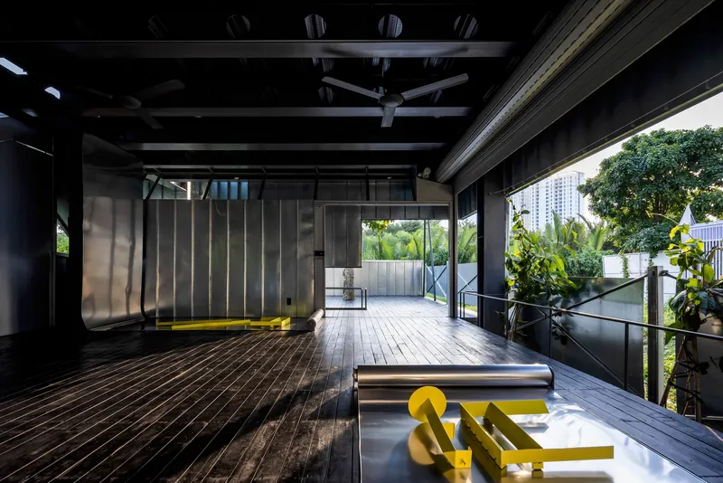 Open-plan interior with exposed steel beams and yellow metal seating overlooking green plantings