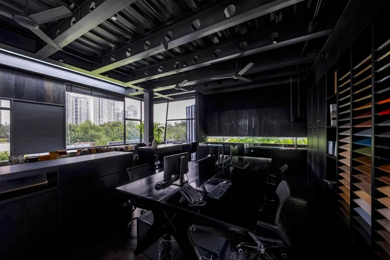 Interior office view showing horizontal window slot framing vegetation and distant towers under exposed rafters