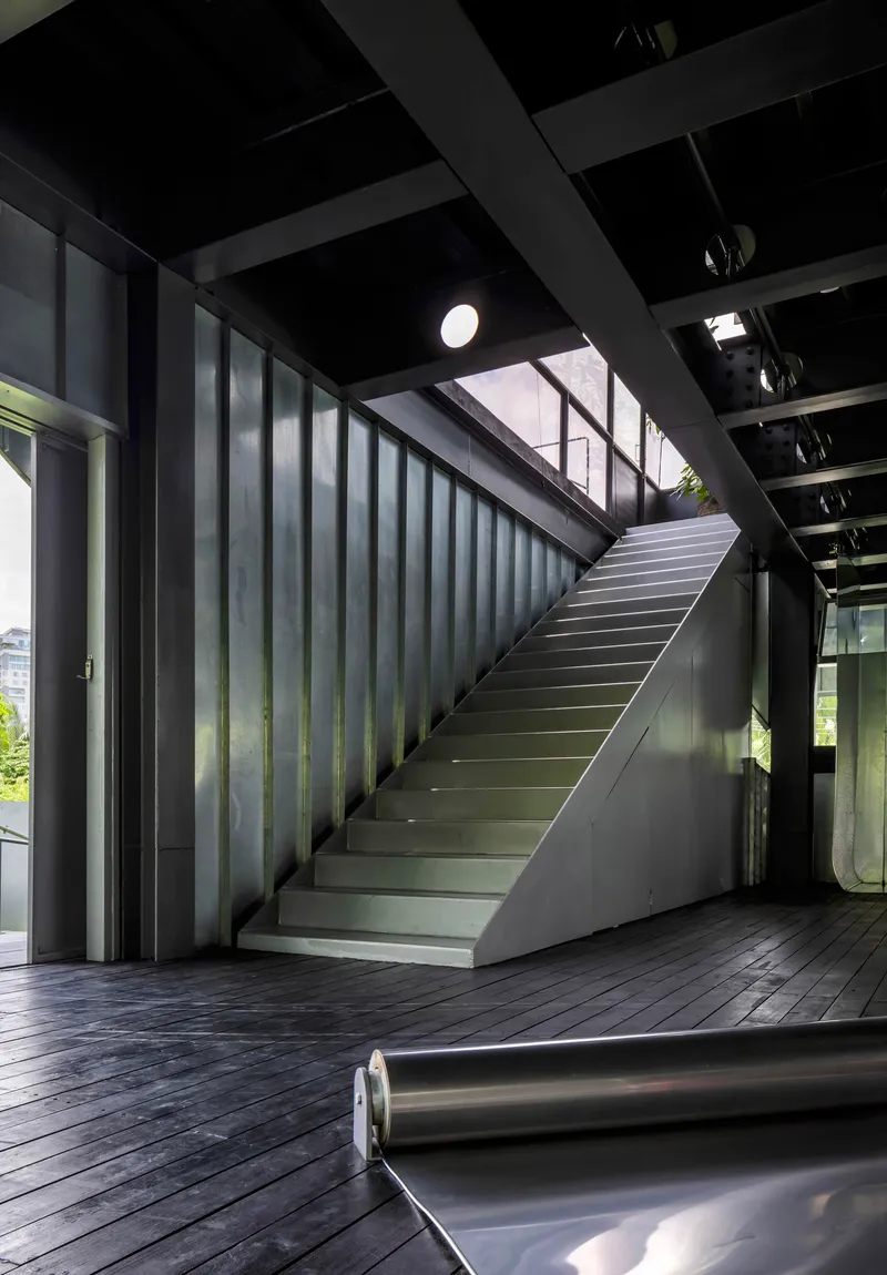 Interior staircase with blackened steel cladding and timber decking under an exposed beam ceiling