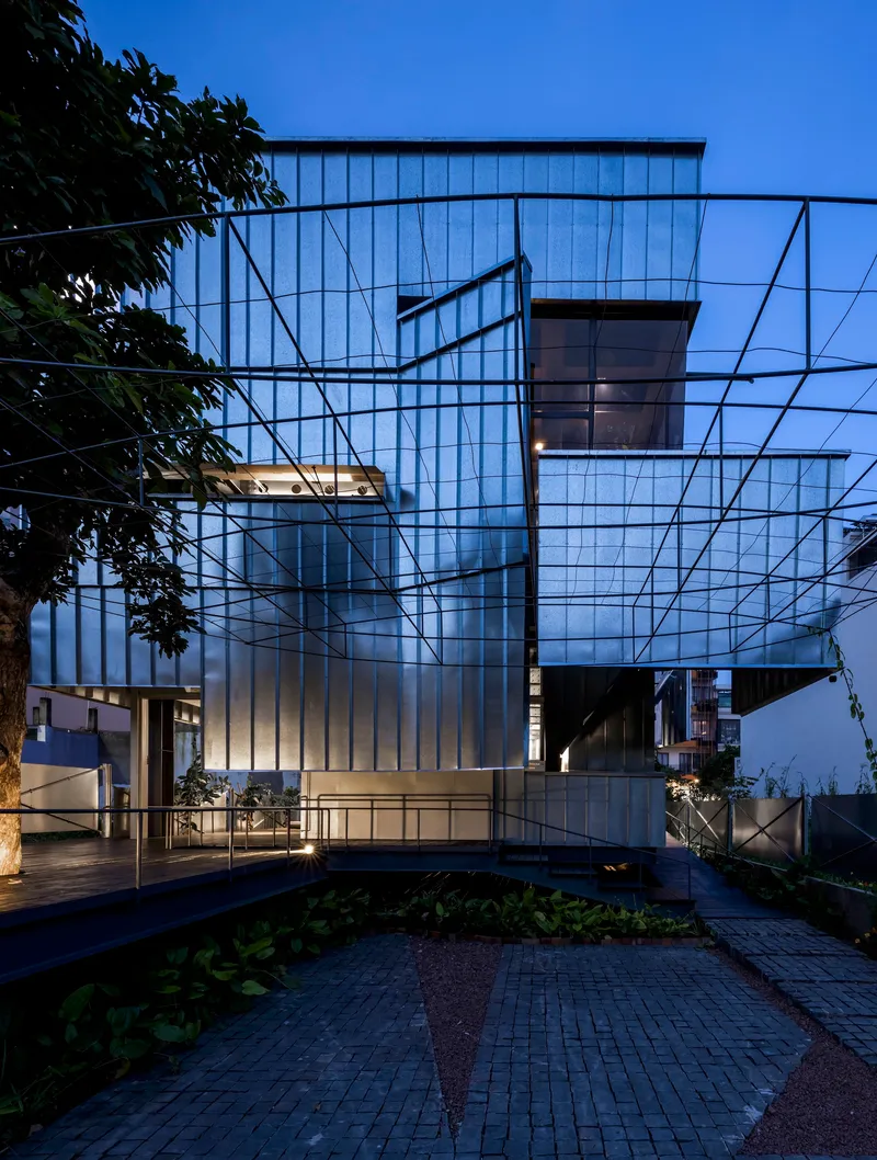 Translucent corrugated facade with steel frame and planted courtyard at dusk