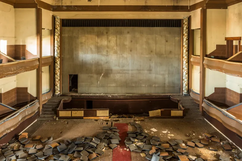 Derelict theater auditorium with tiered seating galleries and ornamental columns flanking the stage