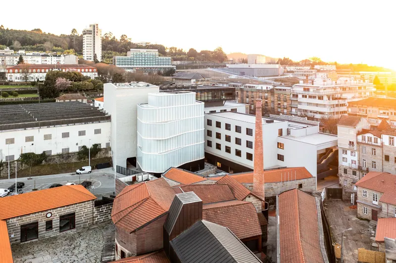 Aerial view of the cylindrical glass volume rising above terracotta rooftops in morning light