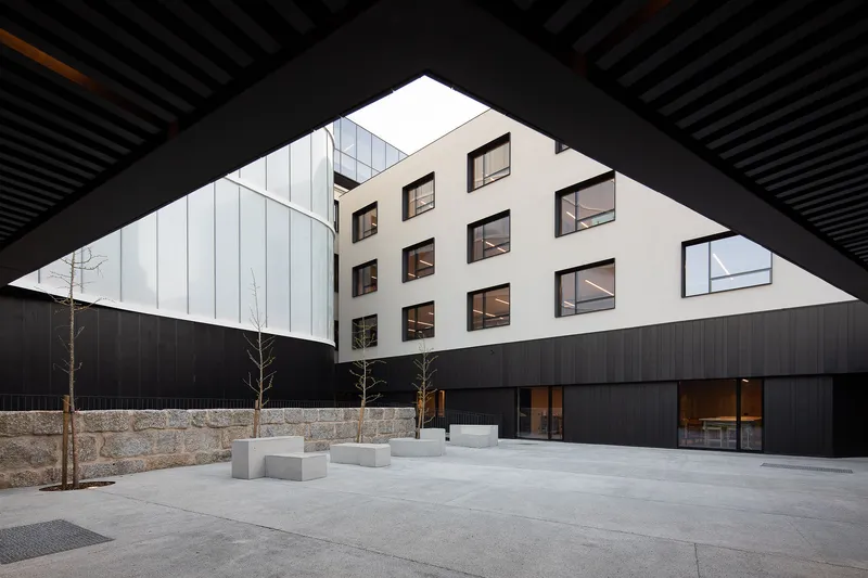 Covered courtyard entry framed by dark slatted ceiling with concrete pavers and young trees below