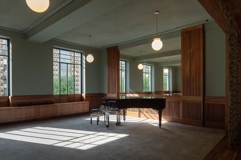 Interior room with grand piano, fluted wood paneling, globe pendant lights and afternoon sunlight streaming across floor