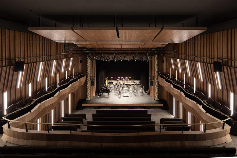 Concert hall interior with curved timber balconies, vertical lit slats and stage set for orchestra