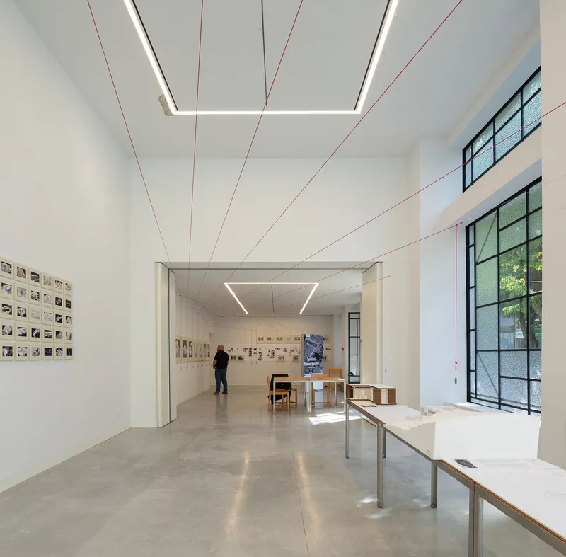 Gallery space with polished concrete floor, red tensioned cables and visitor viewing wall-mounted artworks