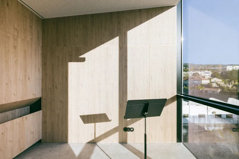 Timber-lined balcony with folding bench and perforated ceiling capturing angular morning light