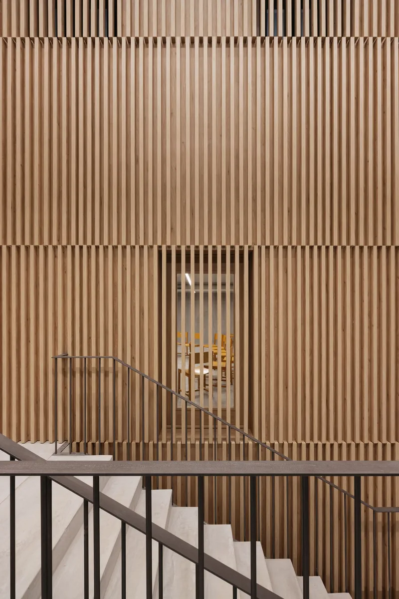 Vertical timber slat wall enclosing a staircase with metal railing and brass handrail