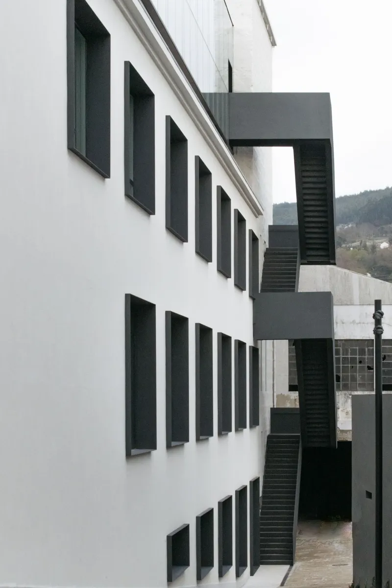 White rendered facade with dark recessed windows and external steel staircase under overcast sky