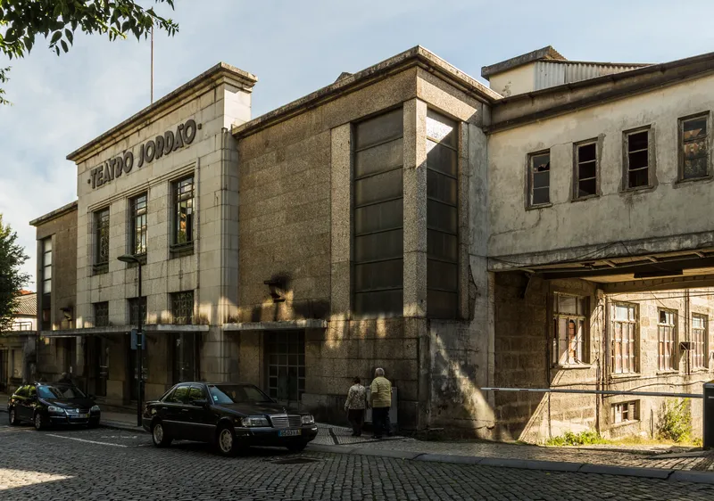 Street facade of the former theater with limestone cladding and two pedestrians passing by