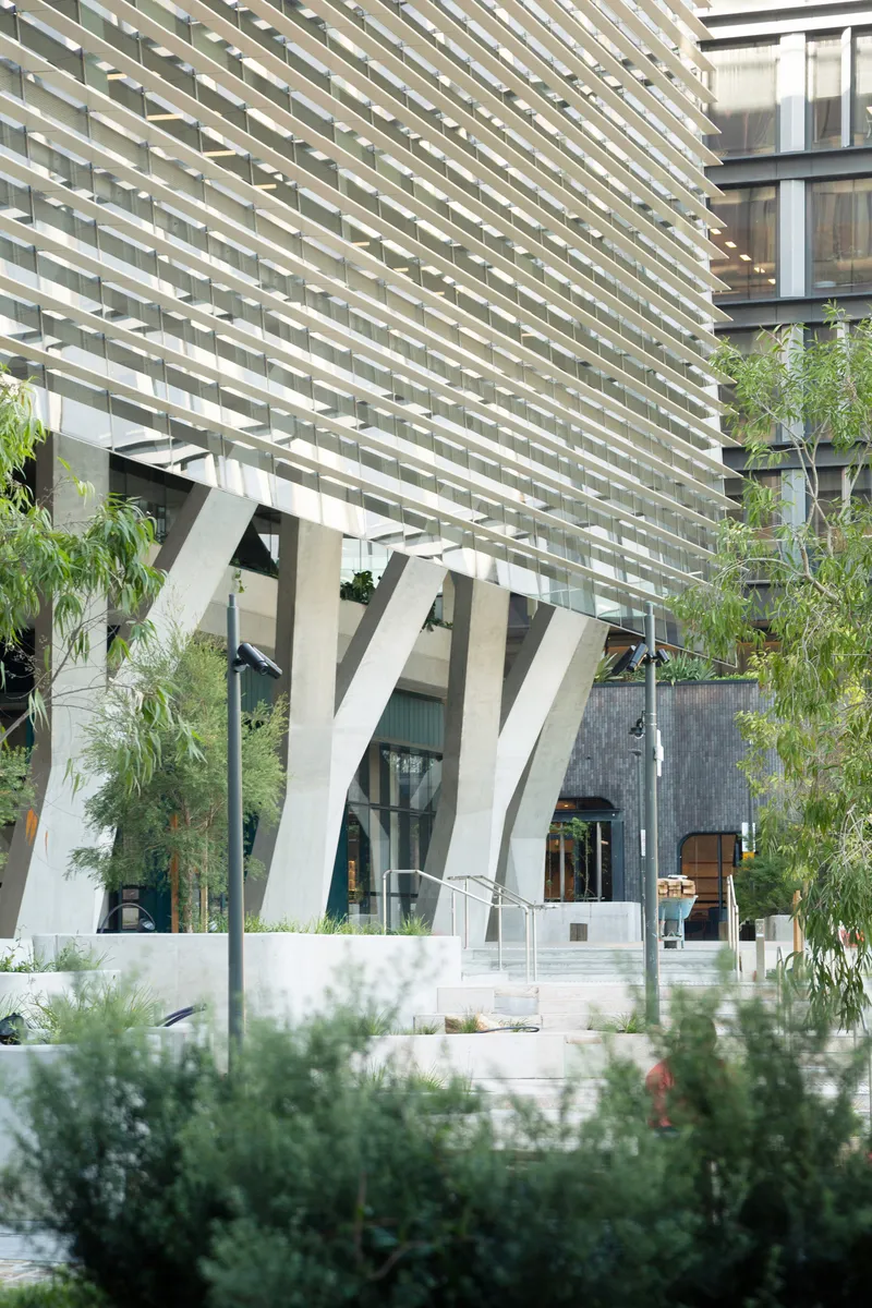 Entry plaza with white branching columns beneath horizontal louvers and landscaped planters