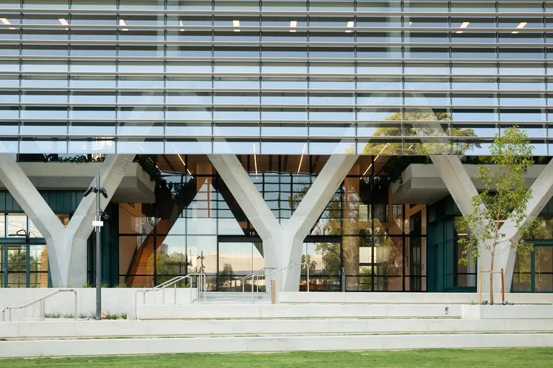 Ground-level view of the branching column system behind glass curtain wall with horizontal sunshades above