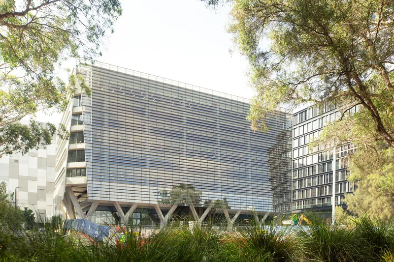 Horizontal louvered facade with V-shaped white columns framed by surrounding trees and native grasses