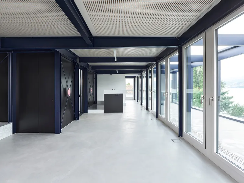 Corridor with floor-to-ceiling glazing, exposed steel beams, and a freestanding dark reception desk