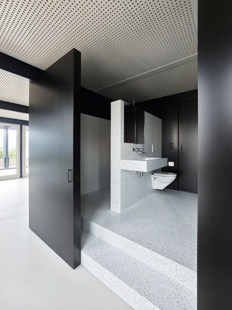 Bathroom with terrazzo flooring, wall-hung sink, and dark metal partition framing the entrance