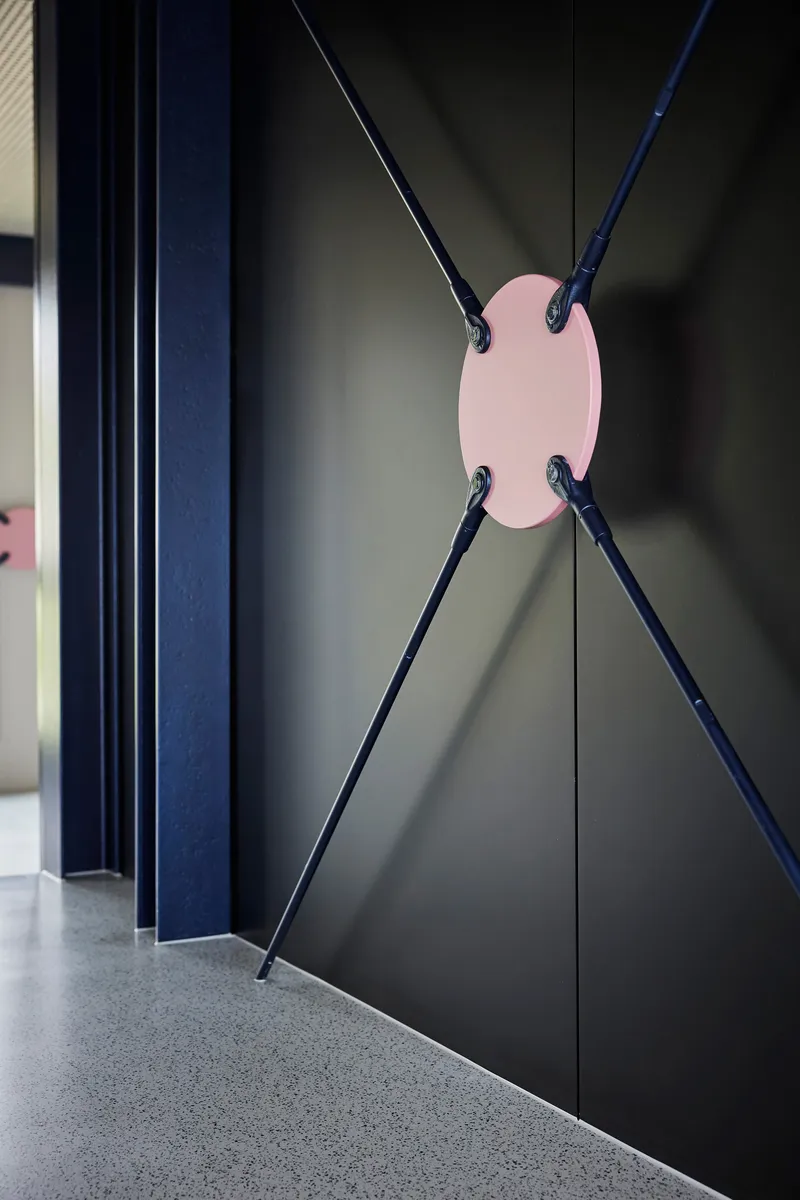 Detail of cable-braced dark metal partition with pink center plate connecting diagonal steel rods