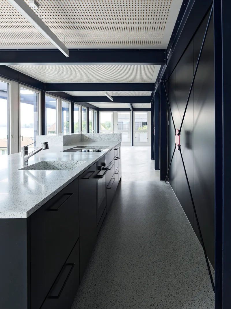 Kitchen with black cabinets, terrazzo countertops, and perforated ceiling panels framed by steel beams