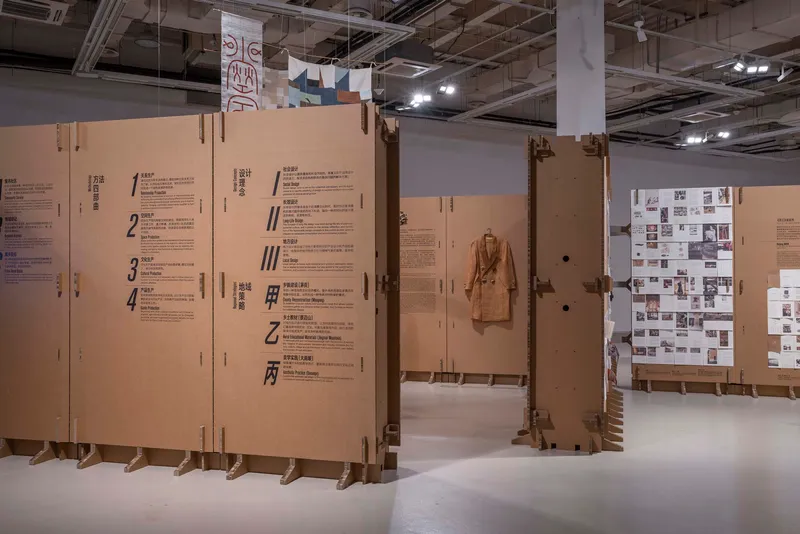 Freestanding cardboard panels with printed text and a hanging garment in a gallery with exposed services