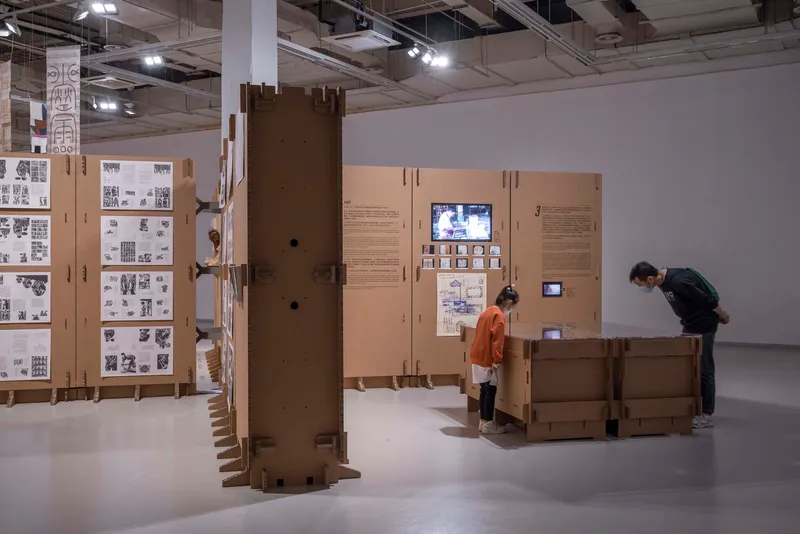 Visitors examining cardboard exhibition units with integrated screens and printed documentation panels