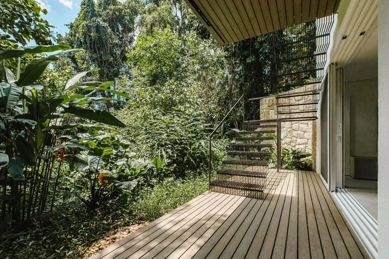 Timber deck with perforated metal staircase rising into dense tropical foliage and banana plants