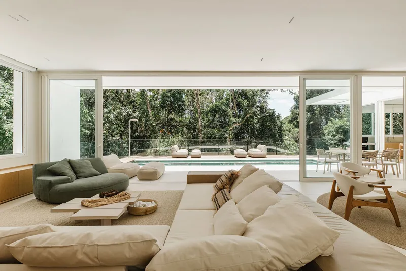 Living room with floor-to-ceiling glass walls overlooking a swimming pool and garden courtyard