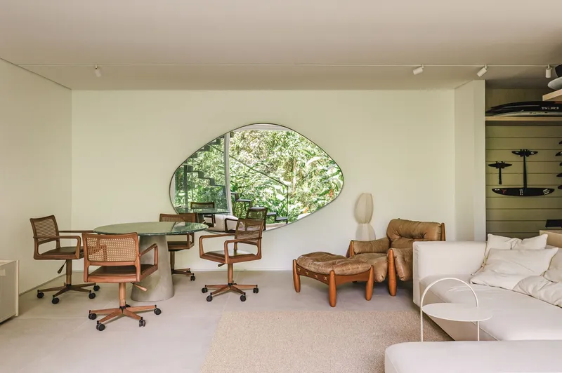Interior space with organic-shaped window opening revealing lush vegetation beyond white walls