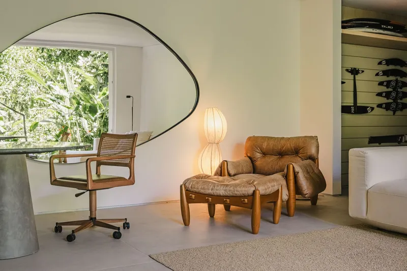 Corner seating area with leather lounge chair beneath a large circular mirror reflecting greenery